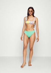 Conjunto de biquíni com parte superior em blocos de cores em tons pastéis de rosa, amarelo e azul, combinado com cuecas de cintura alta em verde menta.