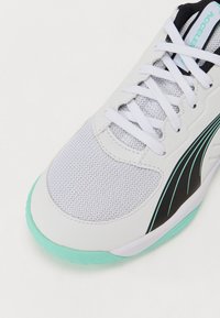 Chaussure de sport blanche avec une tige en maille, accents noirs et bleu-vert, bout rond et semelle texturée bleu-vert. Présente des lacets et un design épuré.