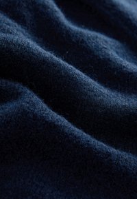 Tissu en laine bleu marine foncé doux avec des fibres visibles et des plis doux créant des ombres texturées et des reflets.