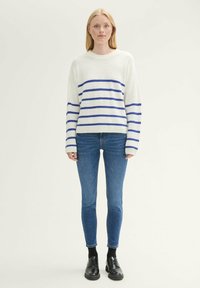 Suéter blanco de punto grueso con rayas horizontales azules, combinado con jeans ajustados azules y zapatos negros con cordones. Diseño y textura simples.