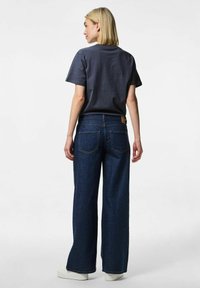 Blue wide-leg jeans feature a high waist, sewn back pockets, and a tan label. Paired with a gray short-sleeve, crew-neck t-shirt.