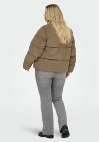 Smeđa proljetna jakna od kordurovog materijala s horizontalnim prošivnim dijelovima, uparena sa sivim proširenim trapericama i crnim glomaznim cipelama. Jednostavna pozadina.