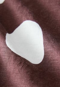 Textília s hlbokohnedou tkaninou s veľkými, nepravidelnými bielymi tvarmi. Materiál sa zdá byť ľahký s hladkým povrchom.