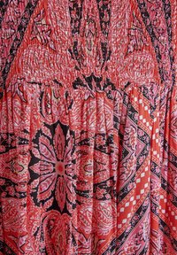 Blommönstrad klänning i nyanser av röd och svart, med smockdetaljer, texturerad tyg och veckade sektioner.