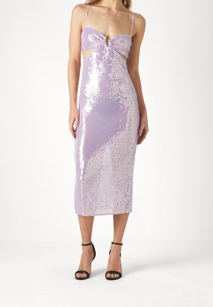 Femme portant une robe midi sans manches en sequins lavande avec des découpes et des talons noirs à bride à la cheville, debout sur fond blanc.