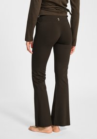 Brązowe rozszerzane spodnie wykonane z elastycznego materiału, z wysokim stanem i delikatnym logo umieszczonym na tylnej części pasa.