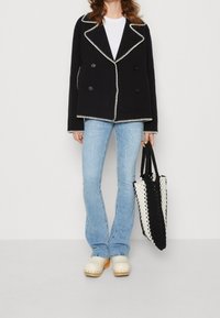 Dubbelzijdig zwart jasje met witte stiksels, lichtgewicht stof, gecombineerd met lichtblauwe flared jeans en een zwart-witte geweven tas.