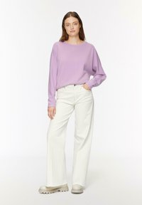 Top de manga larga lavanda combinado con pantalones vaqueros blancos de pierna ancha. Los jeans presentan un dobladillo deshilachado, y los zapatos son beige con una suela gruesa.