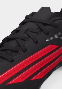 Κοντινό πλάνο μαύρου αθλητικού παπουτσιού με μαύρα κορδόνια και τολμηρό κόκκινο και ασημί ριγέ σχέδιο στη πλευρά.