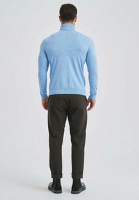 Pull à col roulé bleu clair en tricot doux, associé à un pantalon marron foncé avec revers et des bottines noires. Vue de dos.