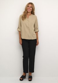Beige linnen blouse met een henley hals en omgeslagen mouwen, gecombineerd met op maat gemaakte zwarte broek en zwarte sleehakken.