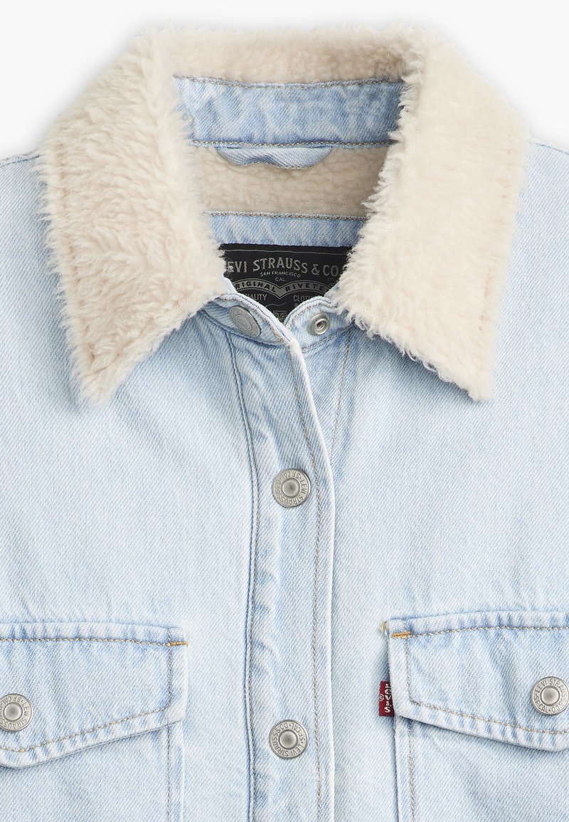 Chaqueta de mezclilla azul claro con un suave cuello beige, dos bolsillos frontales, botones de metal y detalles de costura sutiles.