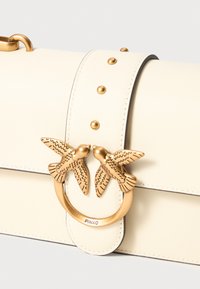 Cream leather handbag with a structured shape, featuring gold-tone bird embellishments and decorative studs along the strap and closure.