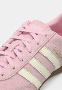 Αθλητικό παπούτσι ροζ σουέντ με τρεις λευκές ρίγες, κορδόνια στο ίδιο χρώμα και χρυσή λεπτομέρεια. Στρογγυλερή μύτη και υφή στο επάνω μέρος για καλύτερο κράτημα.