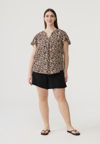 Top a maniche corte con stampa leopardo e scollatura a V, abbinato a pantaloni corti neri. Il tessuto appare leggero e la vestibilità è rilassata. Infradito nere.