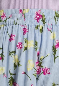 Saia floral azul clara com flores rosas e amarelas. A cintura é pregueada e com textura rçada, feita de um tecido suave e fluido.