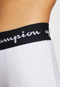 Białe bawełniane szorty z czarnym elastycznym pasem w talii, na którym znajdują się białe napisy „Champion”. Gładka faktura, casualowy design i dopasowany krój.