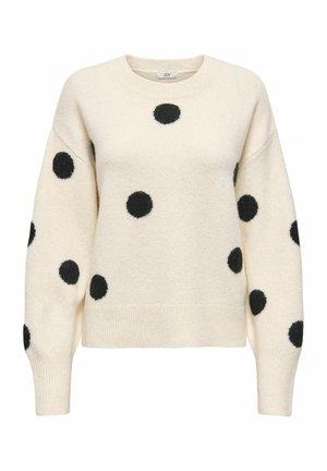 Pull crème avec des pois duveteux noirs, col rond, épaules tombantes, poignets et ourlet côtelés, fabriqué dans une texture douce.