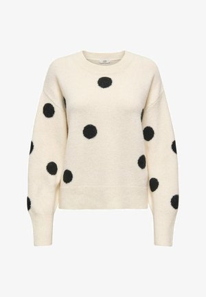 Pull crème avec des pois duveteux noirs, col rond, épaules tombantes, poignets et ourlet côtelés, fabriqué dans une texture douce.