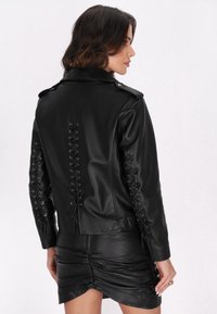 Czarna skórzana kurtka z koronką po bokach i z tyłu, z kołnierzem i guzikami. Gładka tekstura i dopasowany krój.