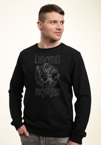 Černá mikina s grafikou zobrazenou s orlem a kytarou, text "LYNYRD SKYNYRD", kulatý výstřih a dlouhé rukávy. Měkká látka.