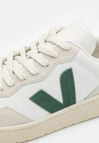 Baskets en cuir blanc avec un logo "V" en daim vert, des accents en daim crème et des lacets blanc cassé ; semelle en caoutchouc texturée.
