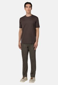 Brahna majica s kratkimi rokavi, v kombinaciji s temno sivimi hlačami slim-fit. Obleko dopolnjujejo svetli športni copati z rjavimi poudarki.
