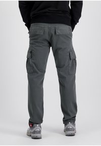 Pantalones cargo de un tejido gris apagado, con dos solapas de bolsillo laterales, un corte relajado y detalles de costura. Combinados con zapatillas deportivas grises.