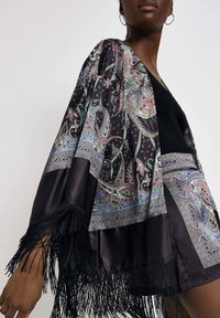 Zwarte satijnen kimono met paisleypatroon in roze en teal, met franjes langs de mouwen en de zoom. Eenvoudig zwart topje eronder.