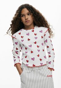 Biely pruhovaný dlhý rukáv s červenými a ružovými vzormi srdca, s červenými volánikmi na okrajoch rukávov. Kombinovaný s pruhovanými nohavicami.