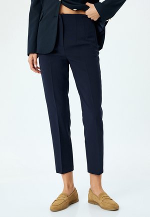 Dark navy tailored trousers with a straight cut, featuring front creases and a mid-rise waist, paired with light brown loafers.