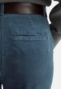Blaue Cordhosen mit einer kleinen Gesäßtasche, strukturiertem Stoff und einem braunen Ledergürtel, der an der Taille sichtbar ist.