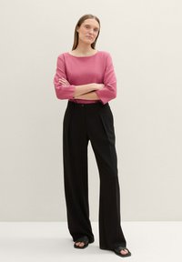 Rózsaszín, hajónyakú pulóver háromnegyedes ujjakkal, magas derekú fekete nadrággal és fekete slip-on szandálokkal párosítva. Sima textúrák.