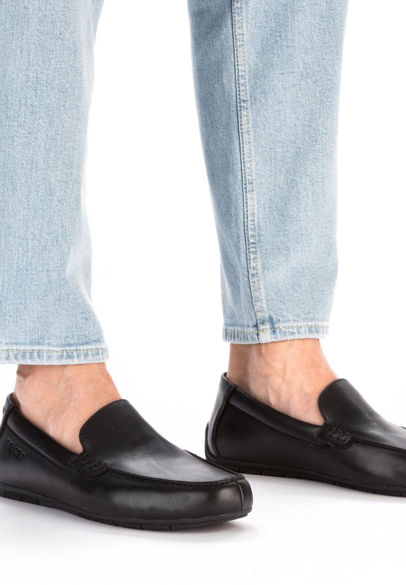 Schwarze Leder-Slipper mit runder Zehenform, glatter Oberfläche und dezenten Nähdetails, kombiniert mit hellblauen Denim-Jeans.