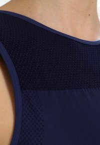 Námořnická bezrukávová halenka s texturovanou síťovinou na ramenou, hladkým materiálem v dolní části a kontrastním lemem kolem výstřihu.