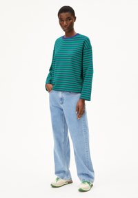 Langärmliges Top in grün und marineblau mit Streifen und Rundhalsausschnitt, kombiniert mit hellblauen, locker sitzenden Jeans und cremefarbenen Sneakers mit grünen Akzenten.