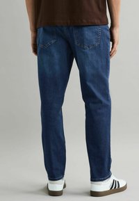 Vaqueros de mezclilla azul oscuro con corte recto, que presentan bolsillos traseros y una ligera textura de lavado, combinados con zapatillas blancas.