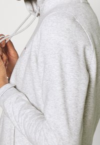 Grau meliertes Zip-Hoodie mit strukturiertem Finish, ausgestattet mit einer verstellbaren Kapuze, gerippten Bündchen und einem kleinen Logo auf der Brust.