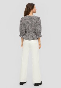 Zwart-wit bloemen peplumtop met uitlopende mouwen, gecombineerd met witte flared jeans en zwarte plateau schoenen. Glad stoftextuur.