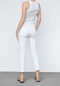 Jeans blancos de corte slim y longitud corta, con dos bolsillos traseros y una cintura de altura media. Combinados con una camiseta sin mangas blanca sencilla.