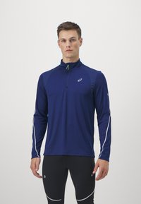 Navy lange mouw sporttop met een ritssluiting aan de kraag, contrasterende witte zijaccenten en een klein logo op de borst en mouw.