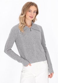 Grijze gebreide cardigan met een rits aan de voorkant, voorzien van een brede kraag, geribde manchetten en kabelbreiaccenten aan de zijkanten. Zachte textuur.