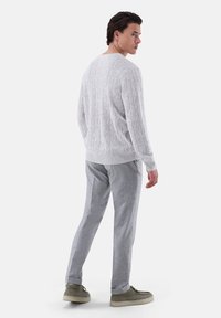 Hellgrauer gestrickter Pullover mit einem strukturierten Muster, kombiniert mit hellgrauen maßgeschneiderten Hosen und beigen Schuhen. Sichtbare Nahtdetails an den Hosen.