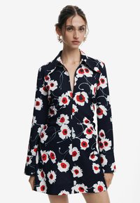 Abito floreale navy con papaveri bianchi e rossi, collo a camicia, maniche lunghe e una vestibilità sartoriale con orlo leggermente svasato.