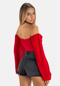 Top rosso off-the-shoulder con maniche lunghe, abbinato a pantaloncini in denim neri a vita alta con orli sfilacciati. Tessuto morbido e design aderente.