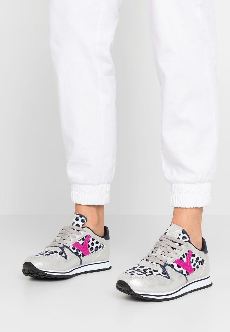 Pieds portant un pantalon de jogging blanc et des baskets grises avec un imprimé léopard noir et blanc et des accents rose vif.