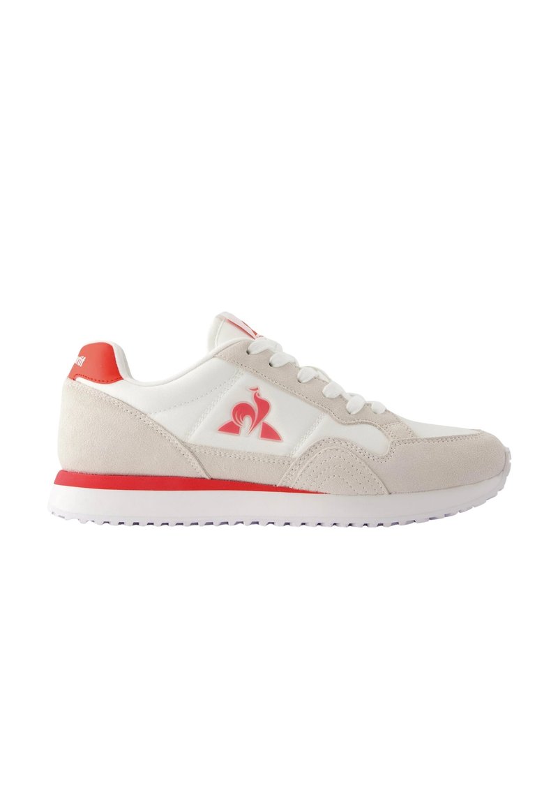 Sneakers en suède beige et synthétique blanc avec des accents rouges, présentant un logo, une silhouette arrondie et une semelle plate avec un motif de texture.