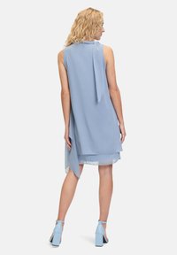 Lichtblauwe, mouwloze jurk met een vloeiende uitstraling, voorzien van een strikdetail op de rug en gelaagd materiaal voor een zachte textuur.