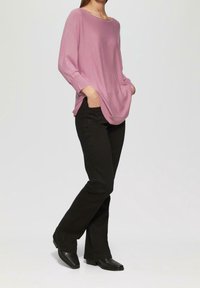 Maglione rosa chiaro, oversize, con scollatura ampia e maniche lunghe, abbinato a pantaloni neri a zampa d'elefante e stivaletti neri.