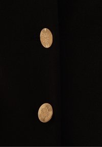Two round gold buttons with intricate raised designs on black fabric, arranged vertically and evenly spaced.